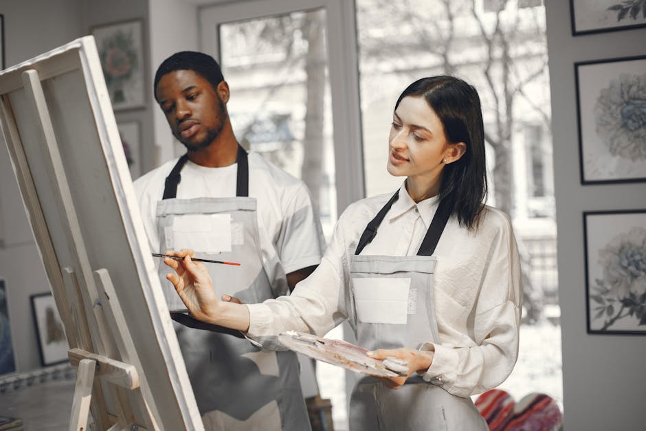 Two artists collaborate in a well-lit studio, focusing on creating art.