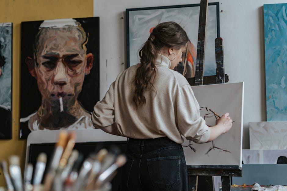 Female artist working on a canvas in a studio with paintings in the background.