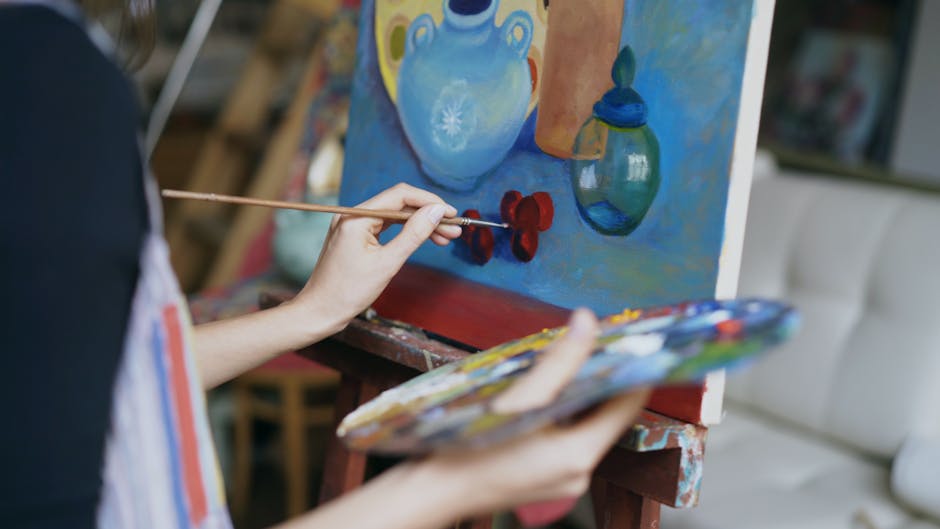 Close-up of an artist's hand painting a colorful still life on canvas in an art studio.