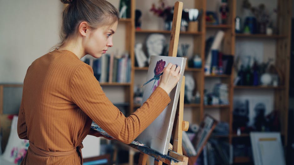 Young female artist painting a rose in her studio, expressing creativity and concentration.